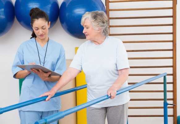 senior-woman-walking-with-parallel-bars-with-therapist
